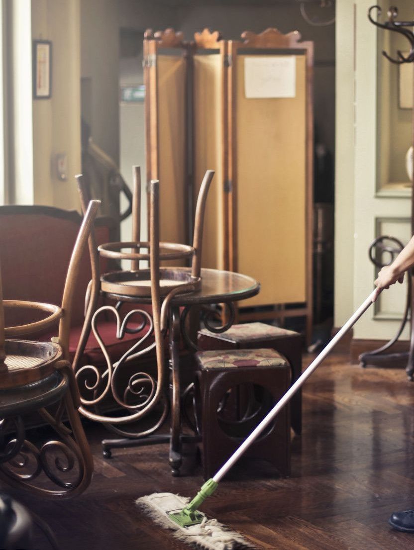 Side view of young ethnic male in uniform cleaning floor with mop while working in retro styled restaurant